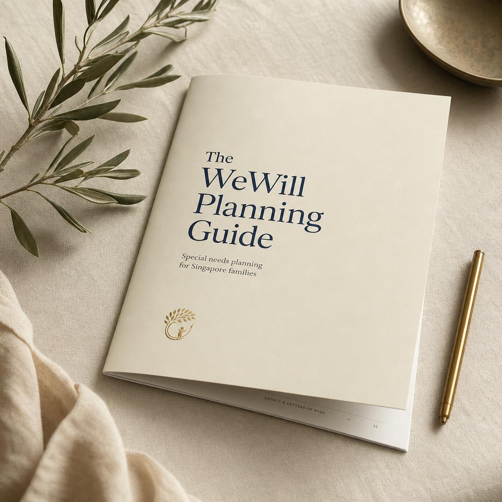 The WeWill Planning Guide booklet resting on a linen surface with olive leaves and a brass pen